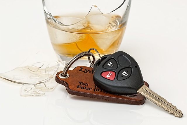 A broken glass with whiskey in it behind a set of keys on a light background.