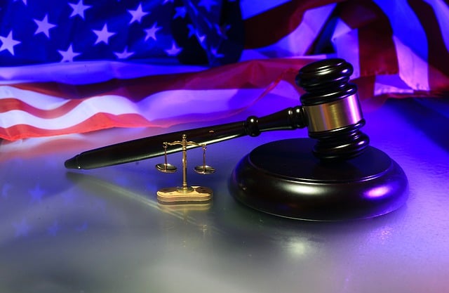 A gavel next to a miniature scales of justice with an American flag in the background.