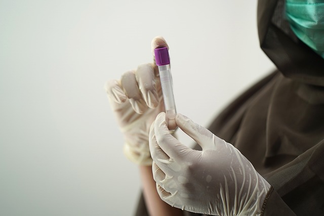 A close up of a nurse with white latex gloves holding a test tube with a clear liquid inside.