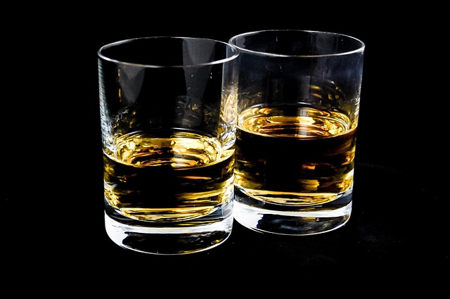 A close up of two glasses half-filled with whiskey on a black background.