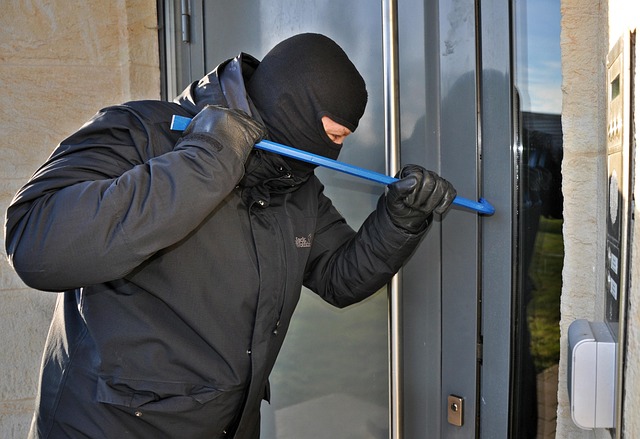 A masked burglar trying to break into a door with a crowbar.