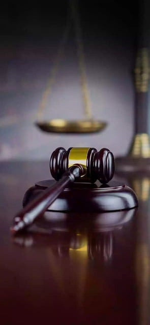 A gavel on a wood surface with the scales of justice in the background.