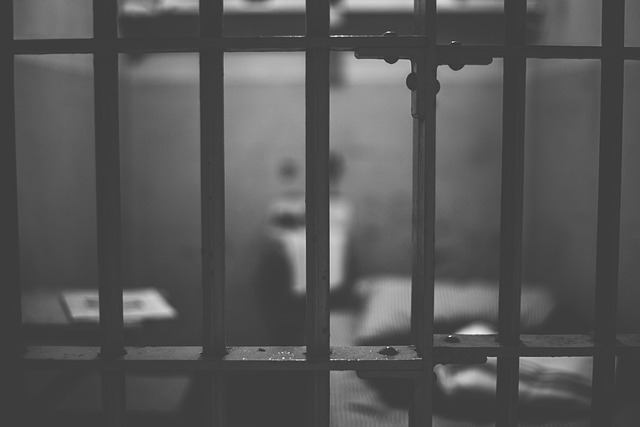 A black-and-white photo of a jail cell with bars in the foreground.